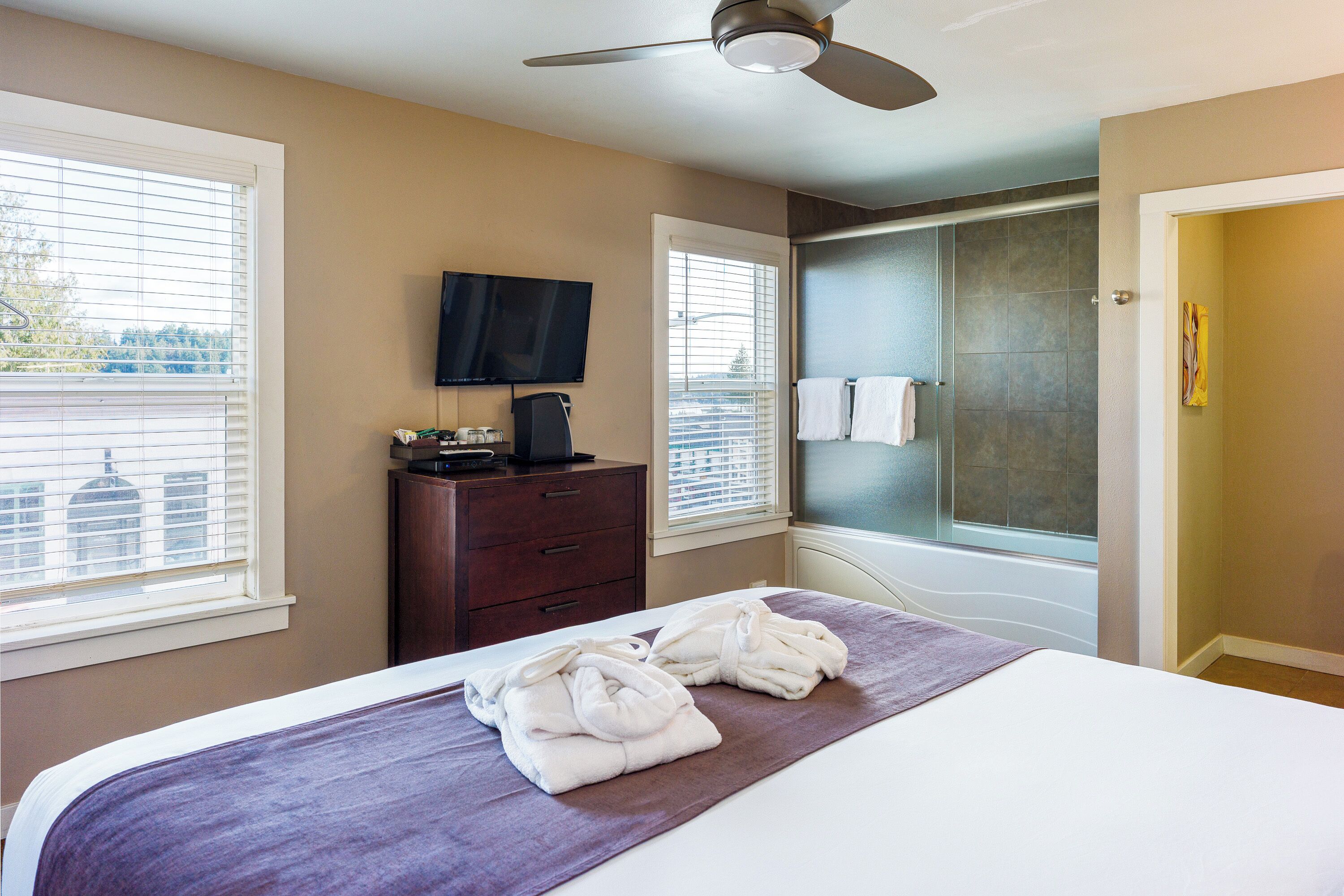 A hotel room with a bed, a television, a desk with a coffee maker, and a shower area.