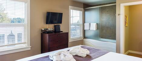 A hotel room with a bed, a television, a desk with a coffee maker, and a shower area.