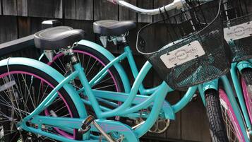 Una bicicleta turquesa con asiento negro y detalles rosados, equipada con una cesta delantera y una etiqueta que dice "Bird Rock Hotel".
