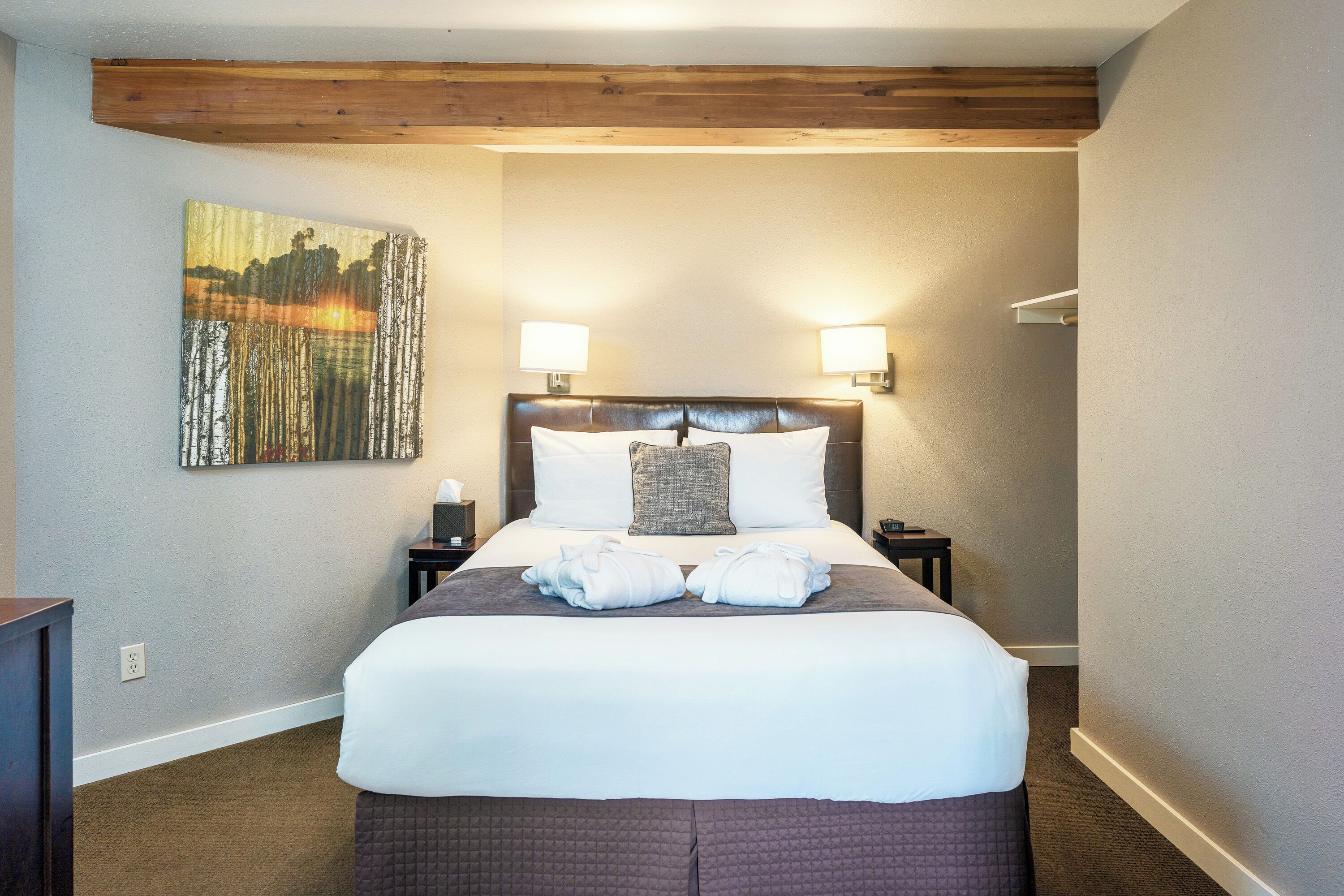 A neatly made bed with white linens, two bedside lamps, and a painting on the wall.