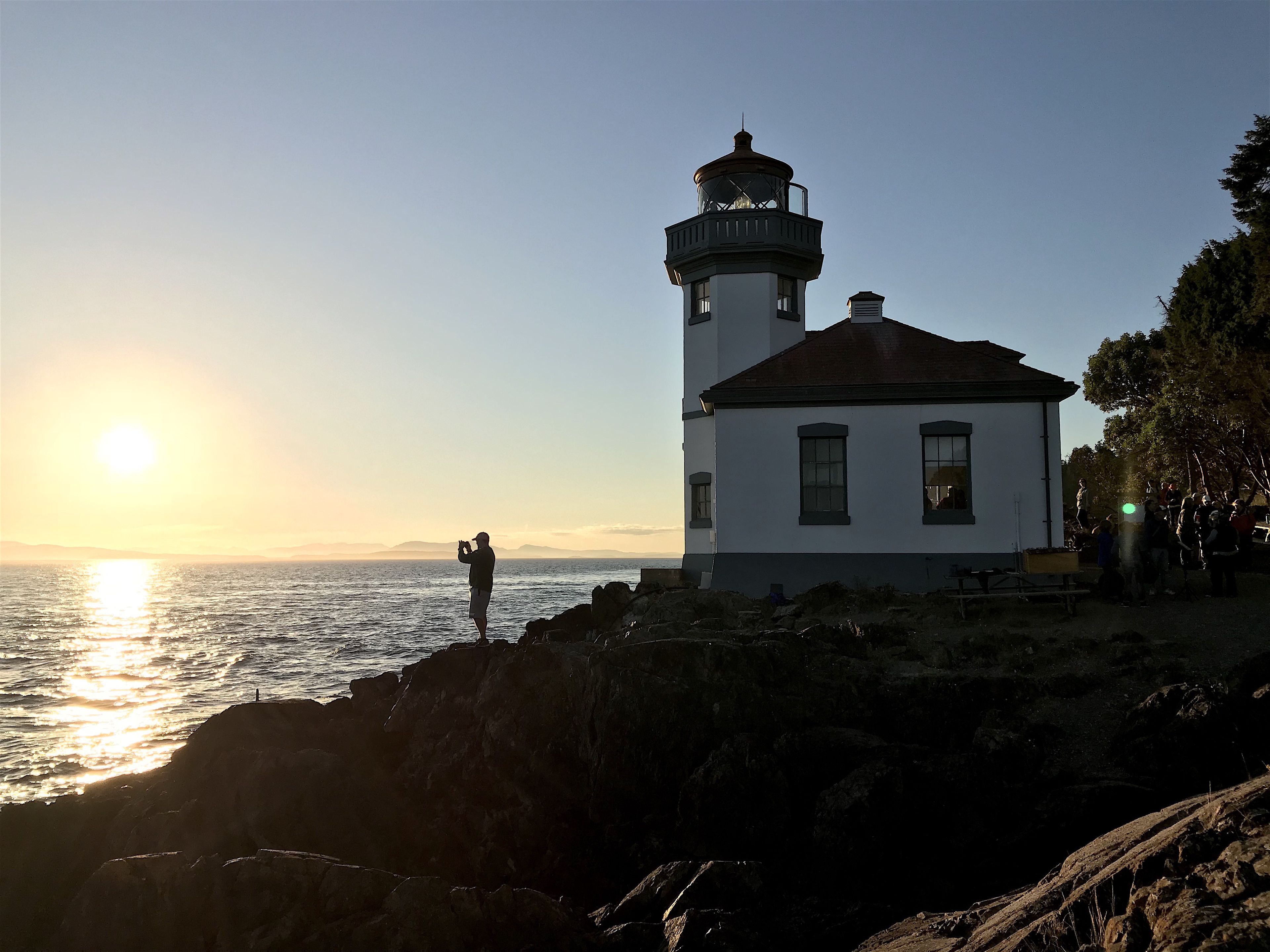 A lighthouse with a white exterior and a red roof, situated on a rocky coastline with the ocean in the background.