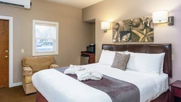 A hotel room with a large bed, a chair, a desk, and a wall-mounted artwork.