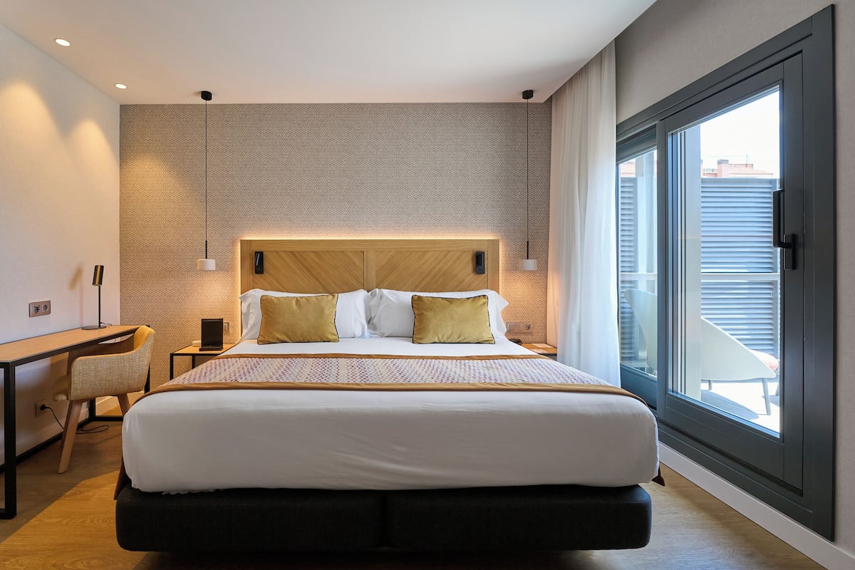 Quarto de hotel moderno com uma cama grande, uma escrivaninha e vista para a cidade pela janela.