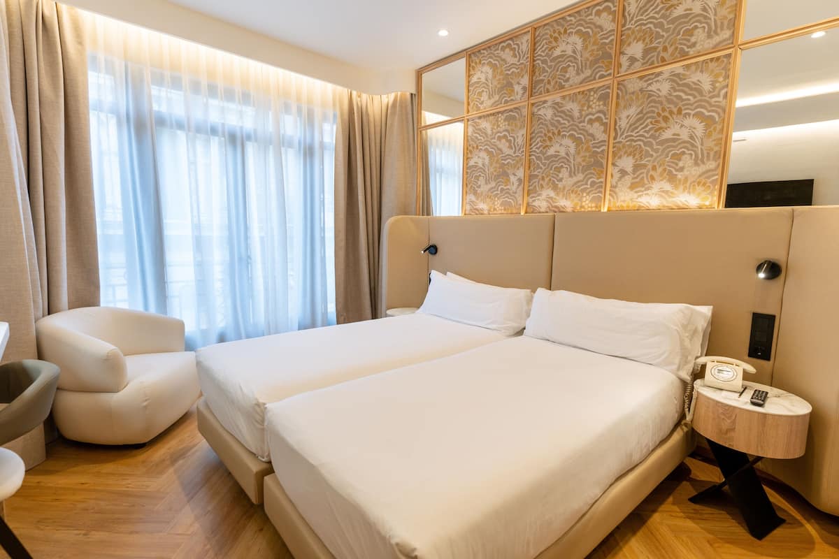 A hotel room with a large bed, a chair, a bedside table with a phone, and a decorative wall panel.
