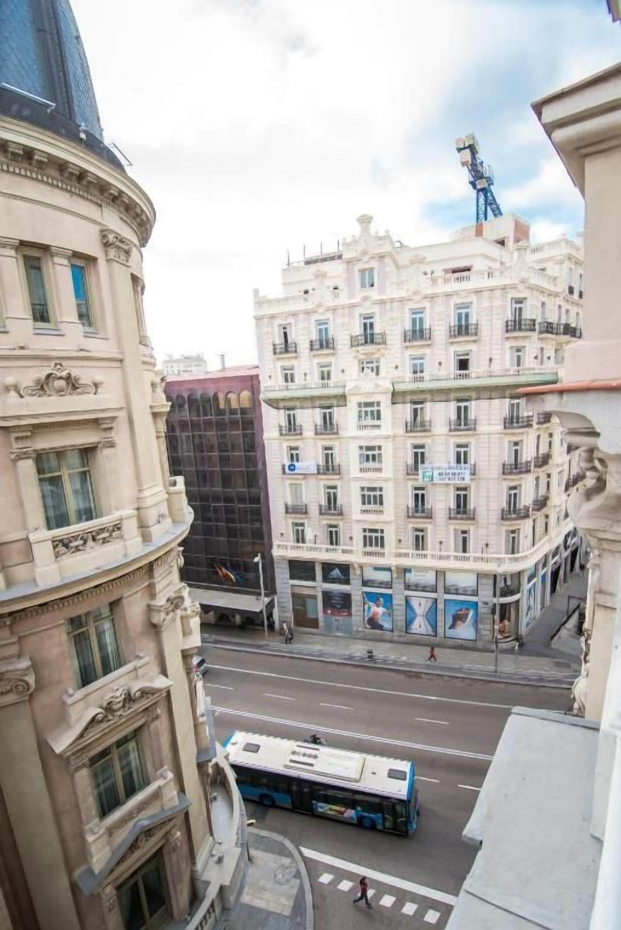 A street view with a building featuring classical architecture, a blue bus, and a pedestrian crossing.