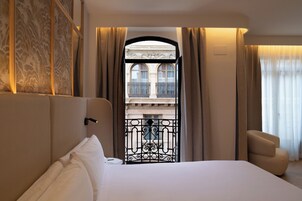 Una habitación de hotel con una cama grande, vistas a un balcón y una zona de estar.