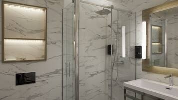 Un baño moderno con ducha envuelta en vidrio, pared con azulejos de mármol, lavamanos blanco y un espejo grande.