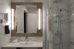 A bathroom with a marble sink, a wooden-framed mirror, and a glass-enclosed shower.