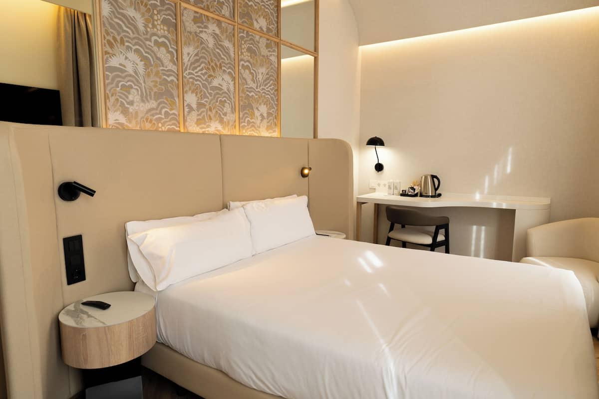 A modern hotel room with a large bed, a desk, and a chair.