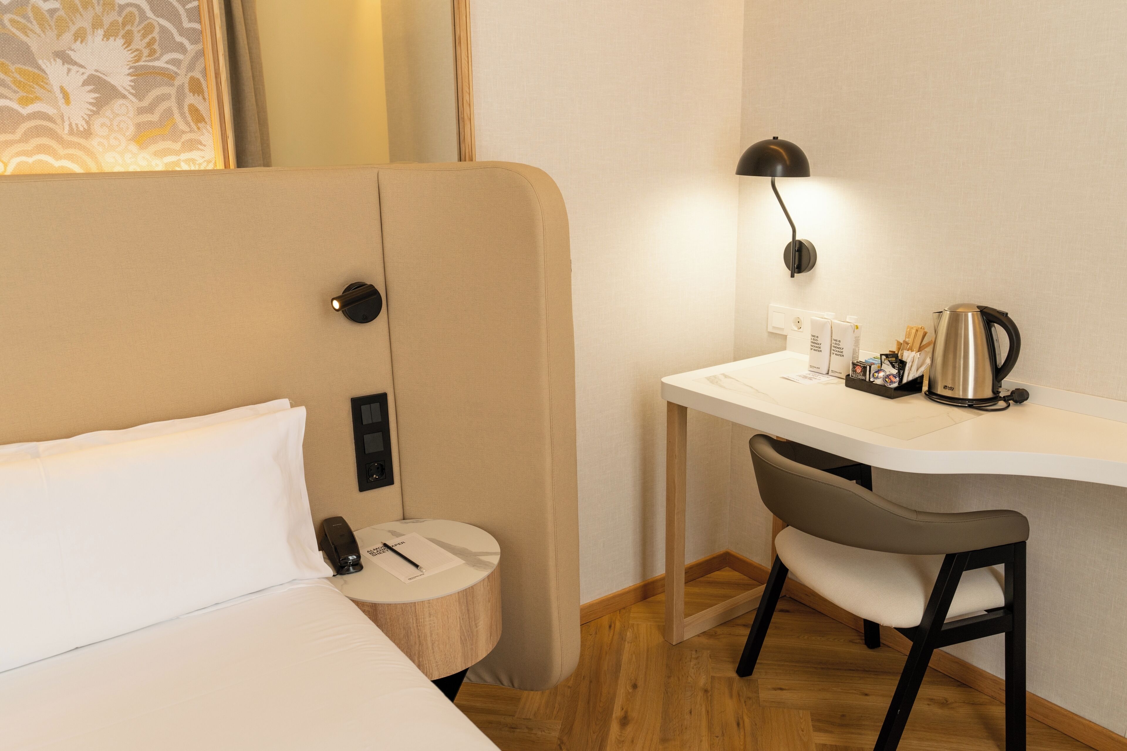 A hotel room with a bed, a desk with a chair, a coffee maker, and a small round table with a lamp.