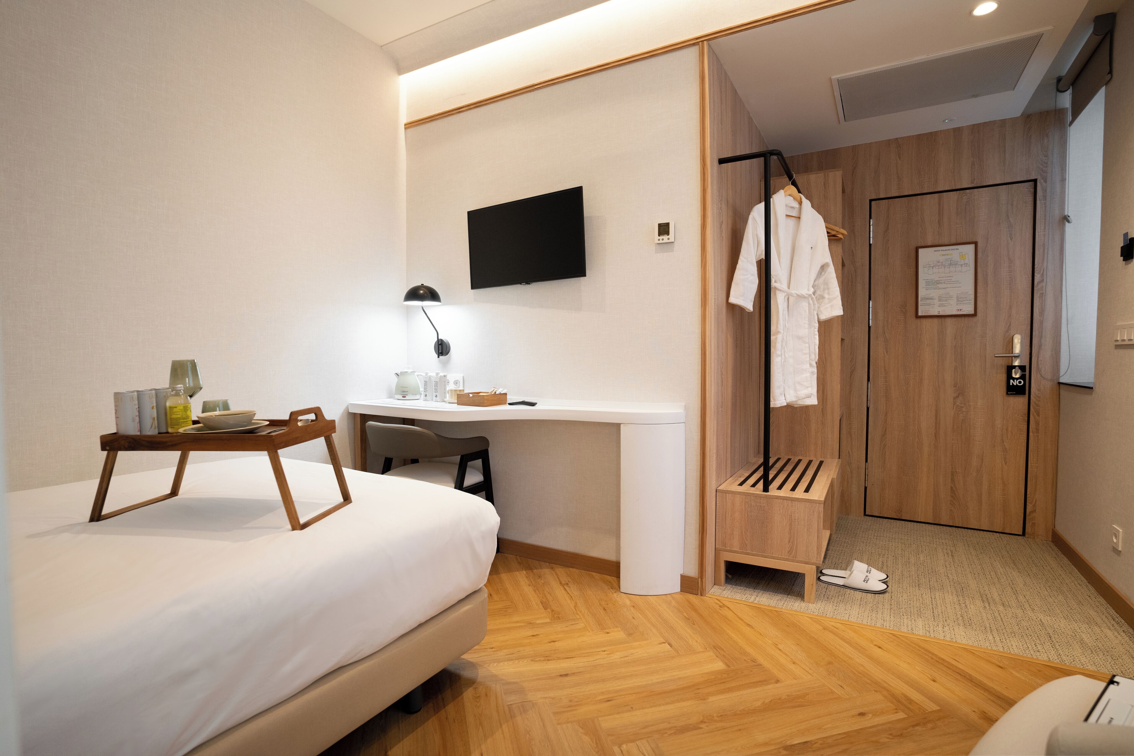 Une chambre d’hôtel comprenant un lit, un bureau avec une chaise, un téléviseur fixé au mur, une armoire en bois et un porte-chaussures.