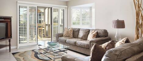A living room with a beige leather sofa, a glass coffee table, and a patterned rug.