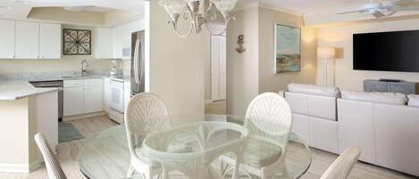 A modern kitchen with white cabinetry, a glass dining table, wicker chairs, and a ceiling fan.