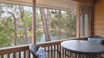 A covered outdoor area with a table and chairs, overlooking a body of water and trees.