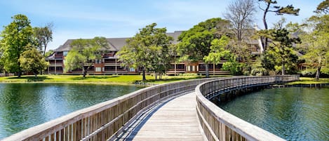 A wooden bridge over a pond with buildings in the background.