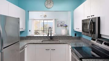 Una cocina con armarios blancos, un refrigerador de acero inoxidable, un microondas y una estufa.