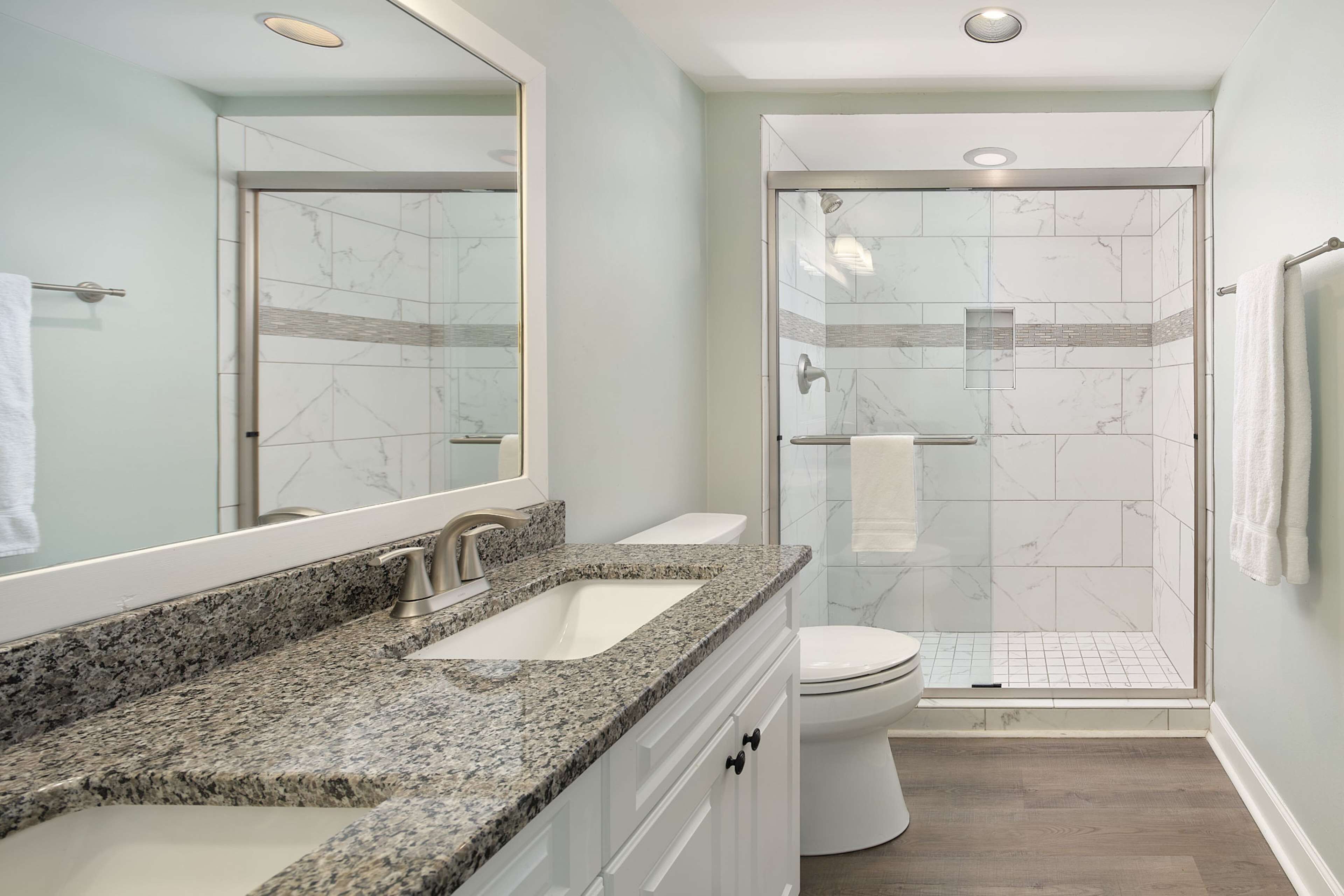 A modern bathroom with a granite countertop, a white sink, a toilet, and a glass-enclosed shower.