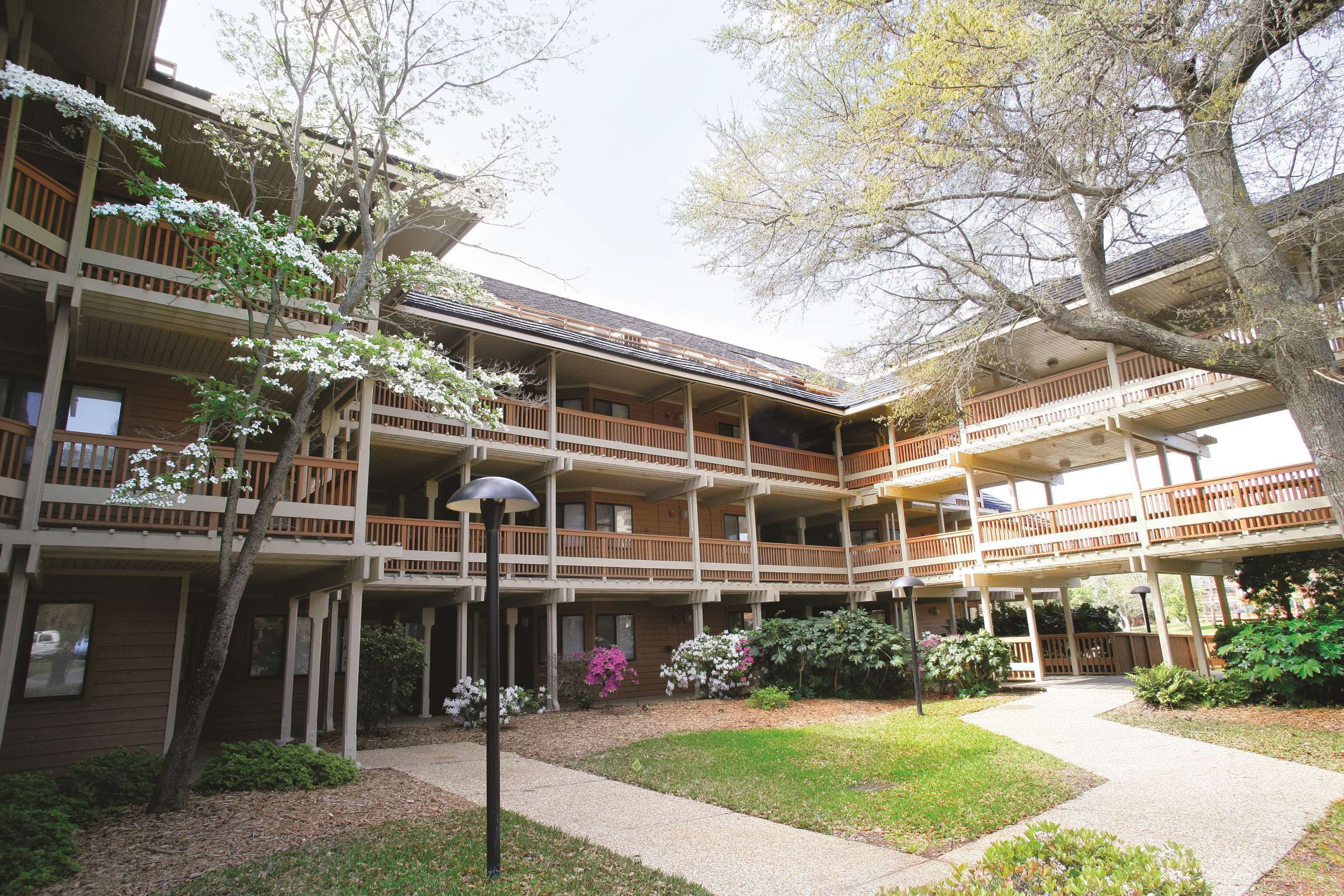 A multi-story building with balconies, a covered walkway, and surrounding greenery.