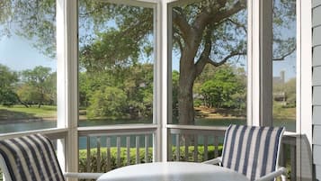 A covered outdoor seating area with a table and chairs, overlooking a natural landscape with trees and a body of water.