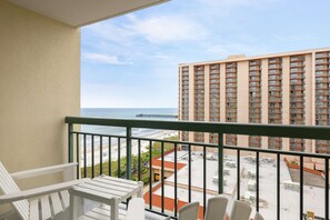 A balcony with white chairs, a view of the beach, and a tall building in the background. - Kingston Plantation Condos (Myrtle Beach)