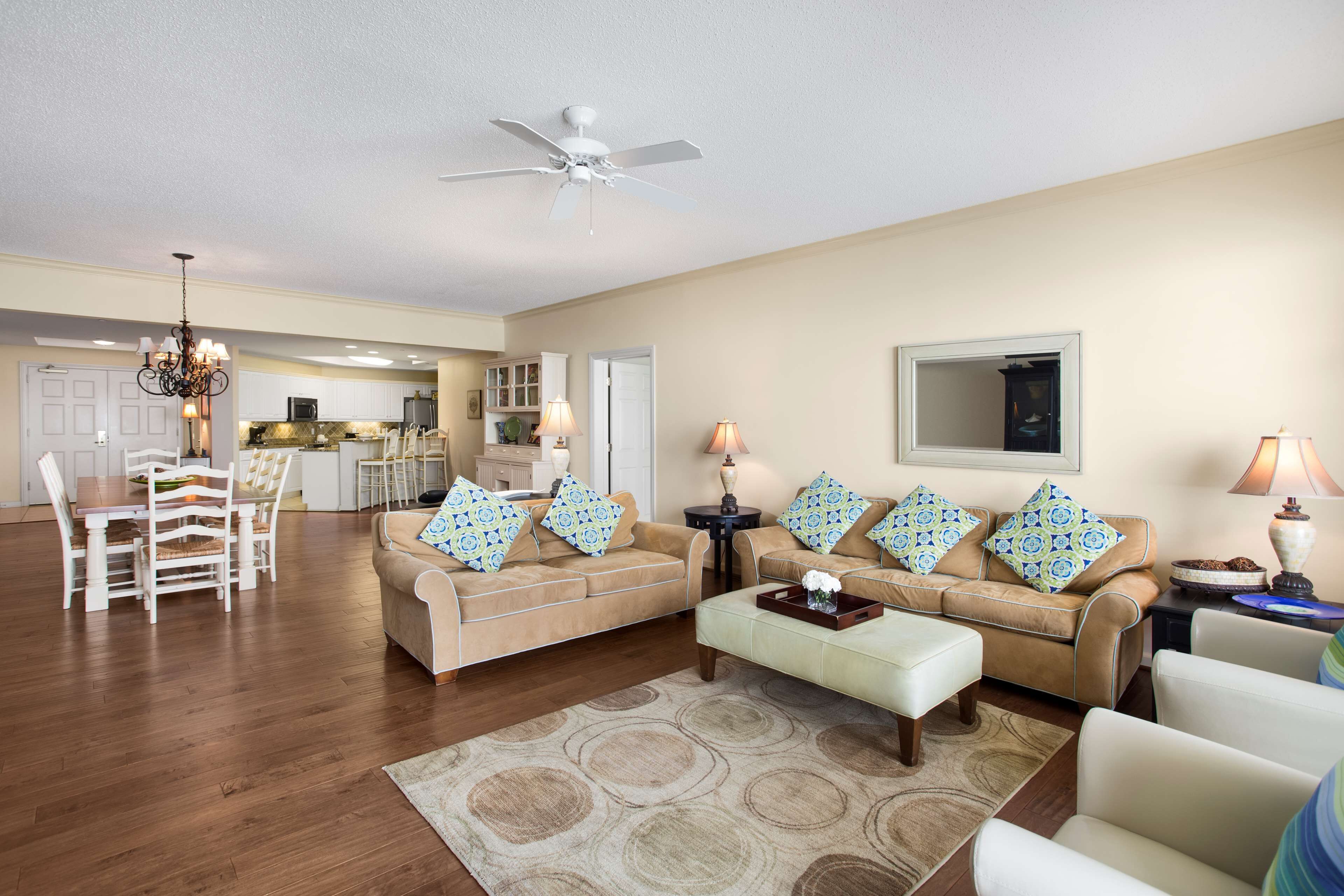 A spacious living room with a beige sofa, a dining area with a wooden table, and a kitchen in the background.