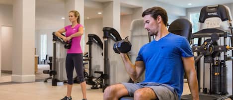 A gym with exercise equipment, a treadmill, and a person using dumbbells.