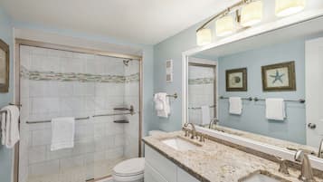 A bathroom with a shower, toilet, sink, and a large mirror.