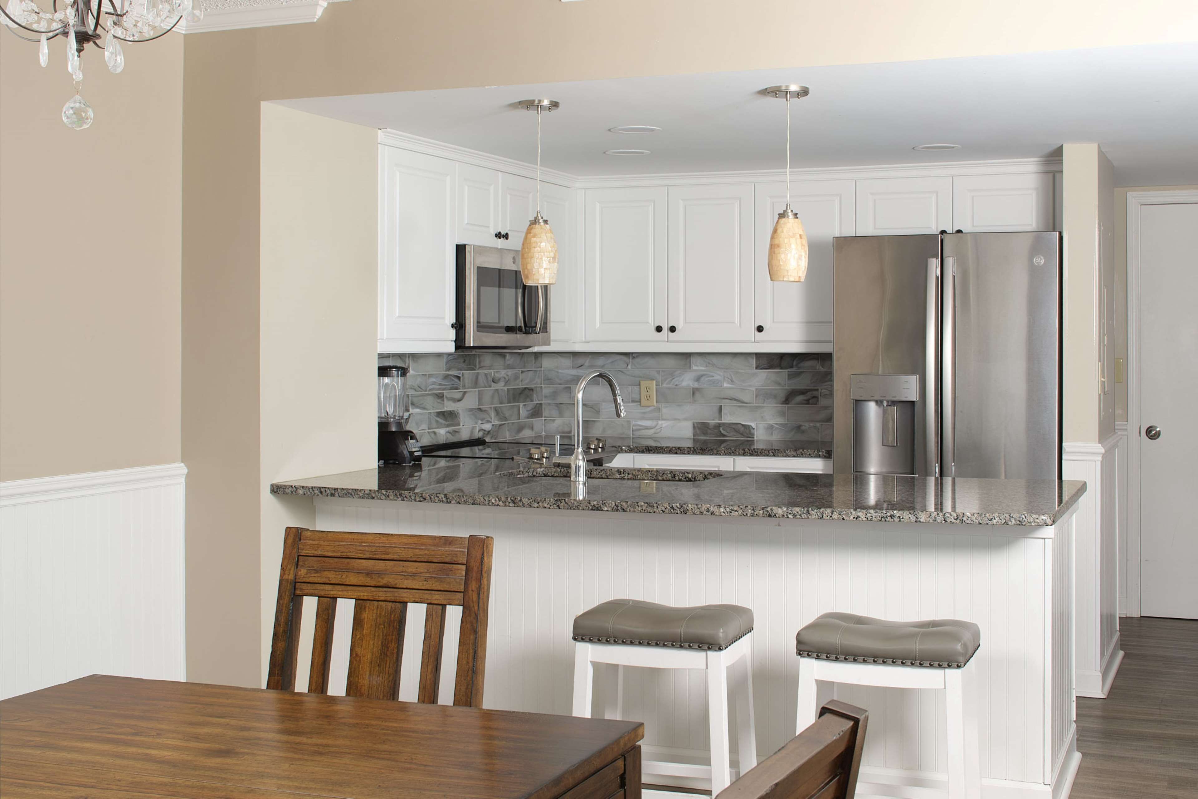 A modern kitchen with white cabinets, a granite countertop, stainless steel appliances, and pendant lighting.
