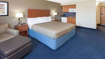 A hotel room with a bed, a desk, a chair, a kitchenette, and a bathroom.