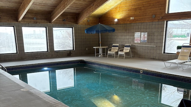 An indoor swimming pool with tiled walls, wooden beams, and a blue umbrella. - AmericInn by Wyndham Webster City (Webster City)