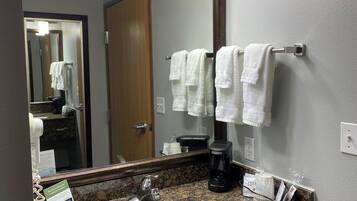A bathroom with a granite countertop, a white sink, a coffee maker, and a towel rack with white towels.