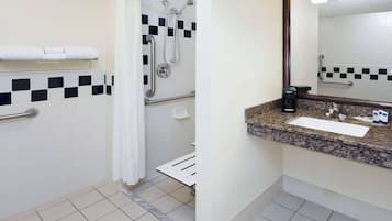 Un baño con ducha, barras de apoyo, lavamanos y espejo.