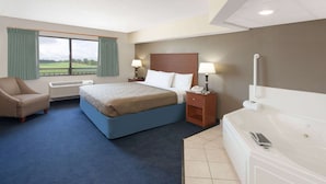 A hotel room with a bed, a chair, a desk, a desk lamp, a telephone, a window with curtains, and a bathtub. - AmericInn by Wyndham Webster City (Webster City)