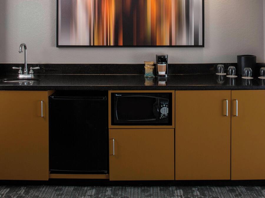 A kitchen with a black countertop, a coffee maker, a microwave, and a sink.