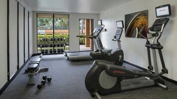 Une salle de sport équipée de tapis de course, de vélos elliptiques, d’haltères et d’un banc de musculation.
