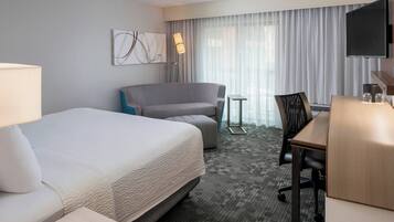 A hotel room with a large bed, a desk, a chair, a TV, and a window with curtains.