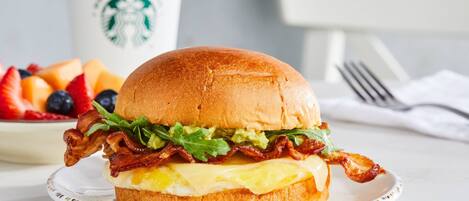 A breakfast sandwich on a plate with a Starbucks cup in the background.