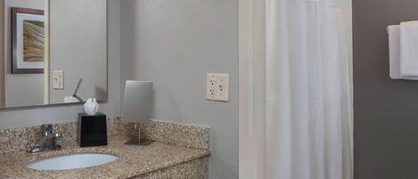 Un baño con lavamanos de encimera de granito, espejo, toallero y cortina de ducha.