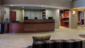 A hotel lobby with a reception desk, a seating area with a striped sofa, and a small kitchenette. - Courtyard by Marriott Daytona Beach Speedway/Airport (Daytona Beach)