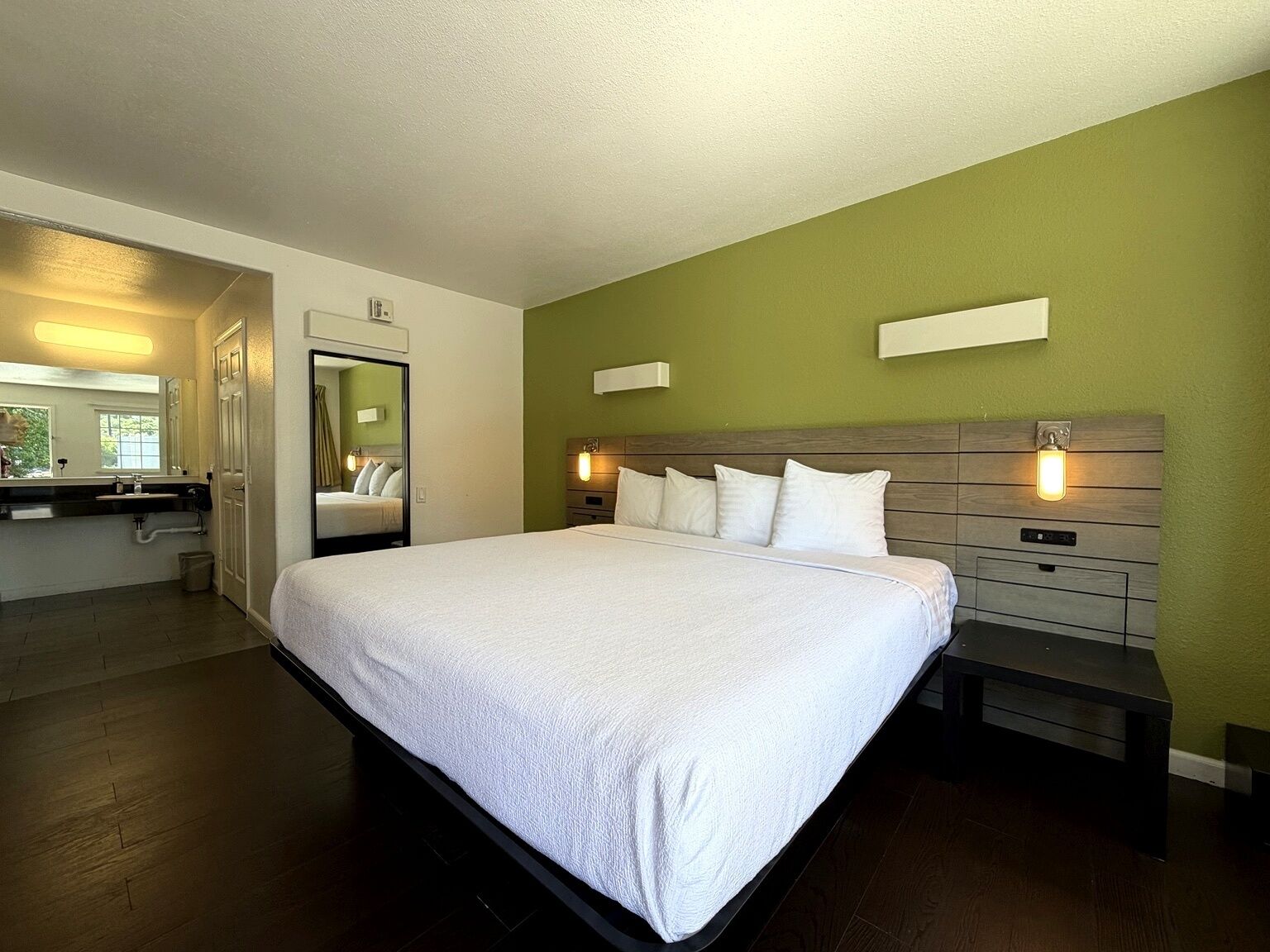 A hotel room with a large bed, bedside tables, a mirror, and a view of the bathroom.