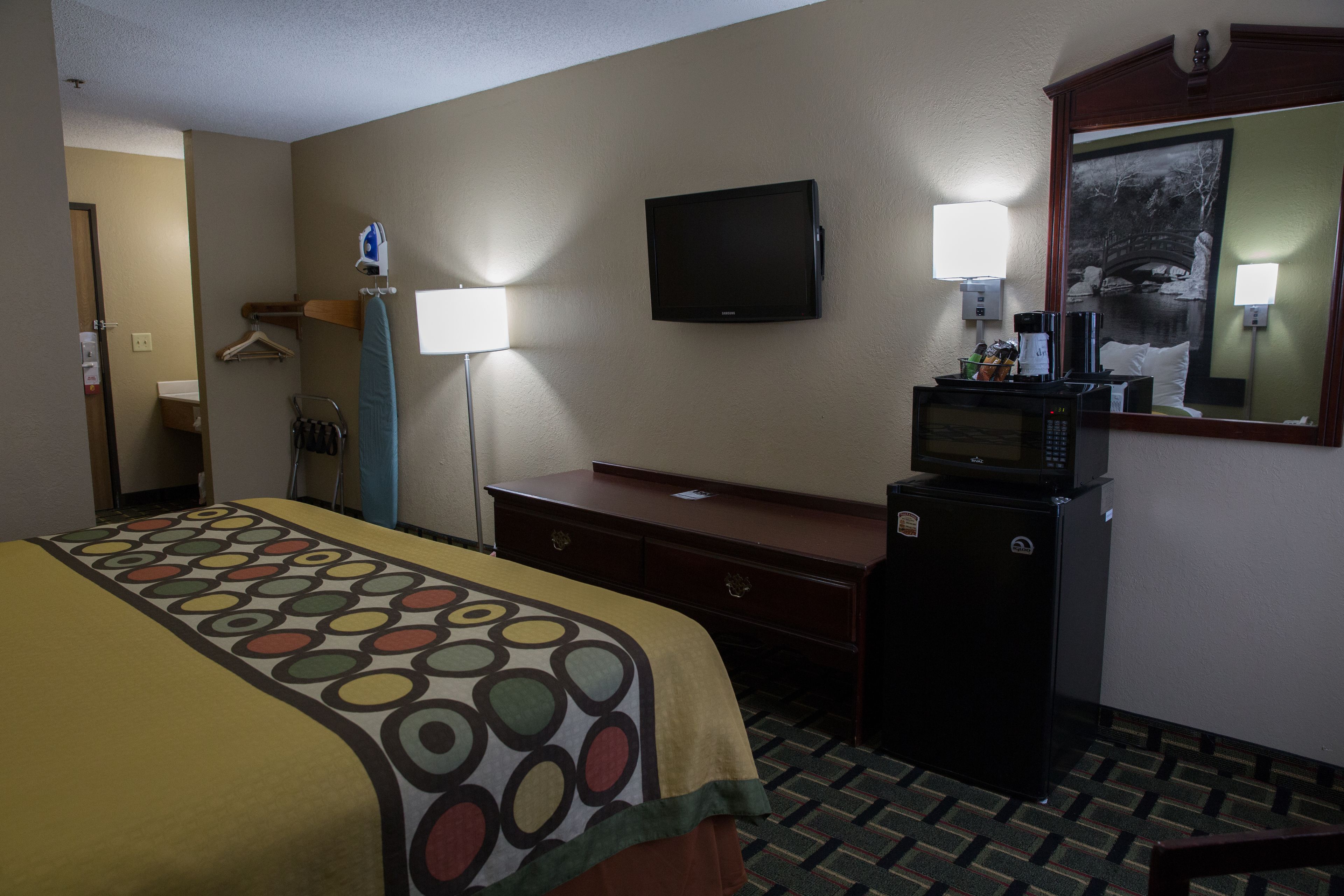 Una habitación de hotel con cama, escritorio, televisor, microondas y espejo.
