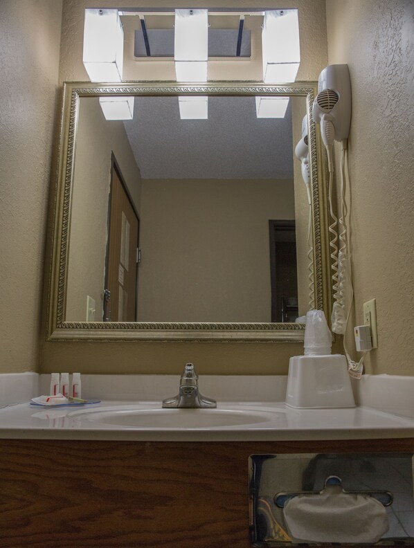 A bathroom with a large mirror, a hairdryer, and toiletries on the sink. - Econo Lodge Canton North (Canton)