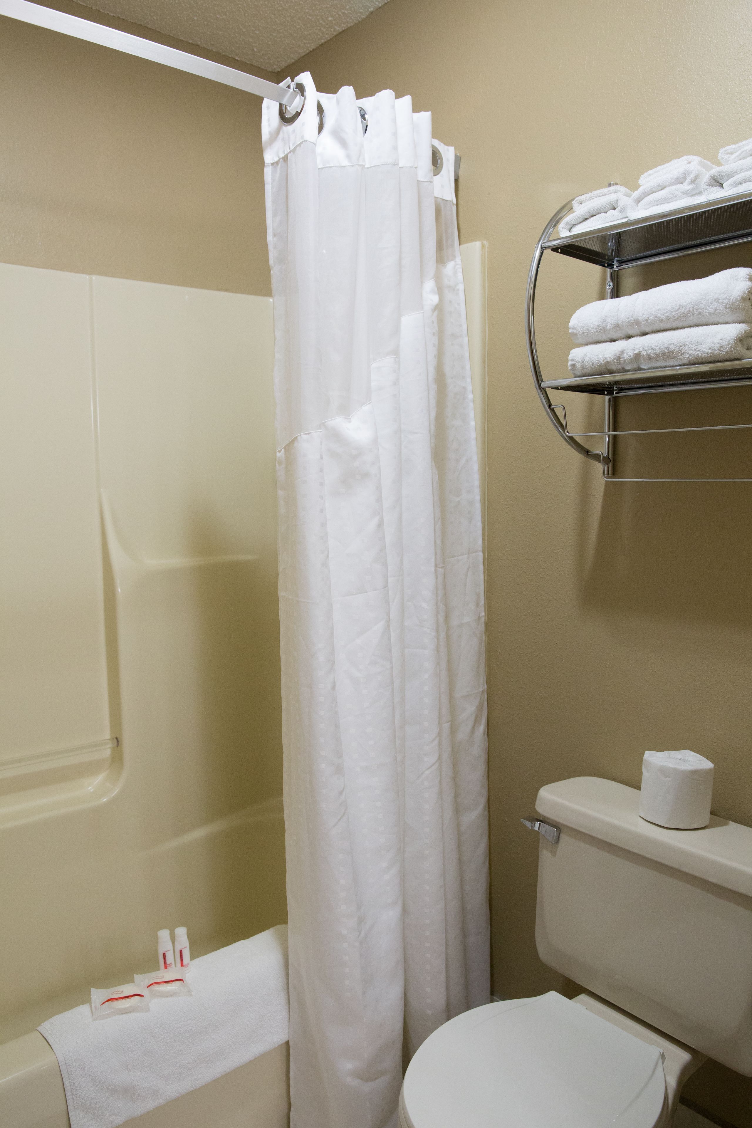Een badkamer met douchegordijn, toilet, handdoekrek met handdoeken en toiletartikelen op de vloer.