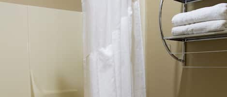 Een badkamer met douchegordijn, toilet, handdoekrek met handdoeken en toiletartikelen op de vloer.