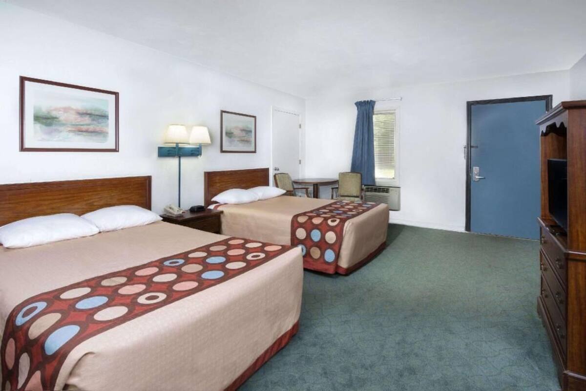 A hotel room with two beds, a desk, a chair, a lamp, and a wardrobe.