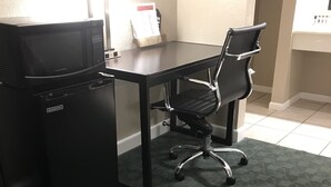 A compact office space with a black desk, a black office chair, and a black refrigerator.