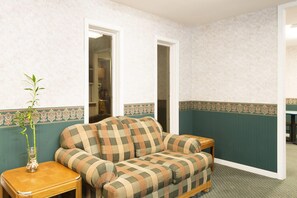 Una habitación con un sofá a cuadros, una mesita de madera, un florero con una planta y un borde decorativo en las paredes.