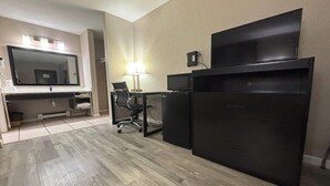 A hotel room with a large bed, a desk with a computer, a TV, and a mirror.