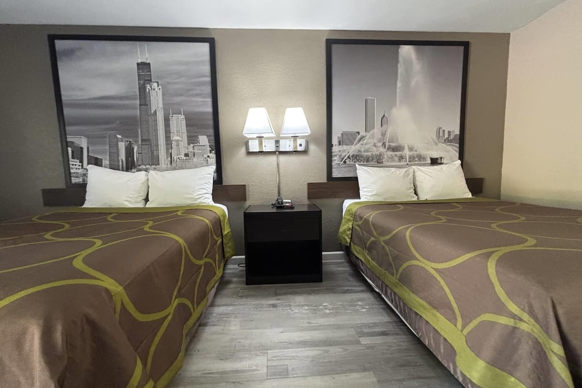 A hotel room with two beds, a nightstand with lamps, and two large cityscape posters on the walls.