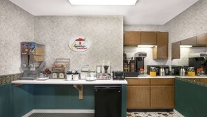 A compact kitchen with a breakfast station, a coffee machine, and a refrigerator.